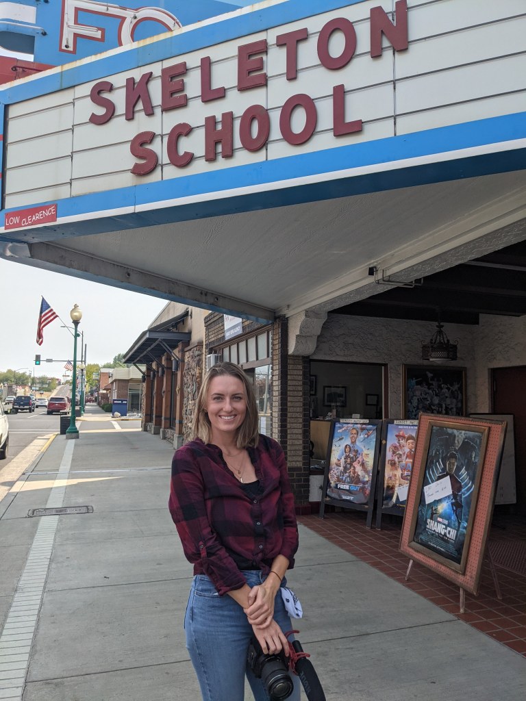 Lauren Paterson stands under a theater marquee which reads "skeleton school."