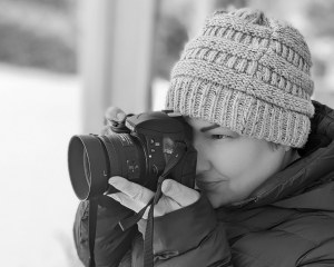 Niki holds a black camera up to her eye in this black and white photo. 